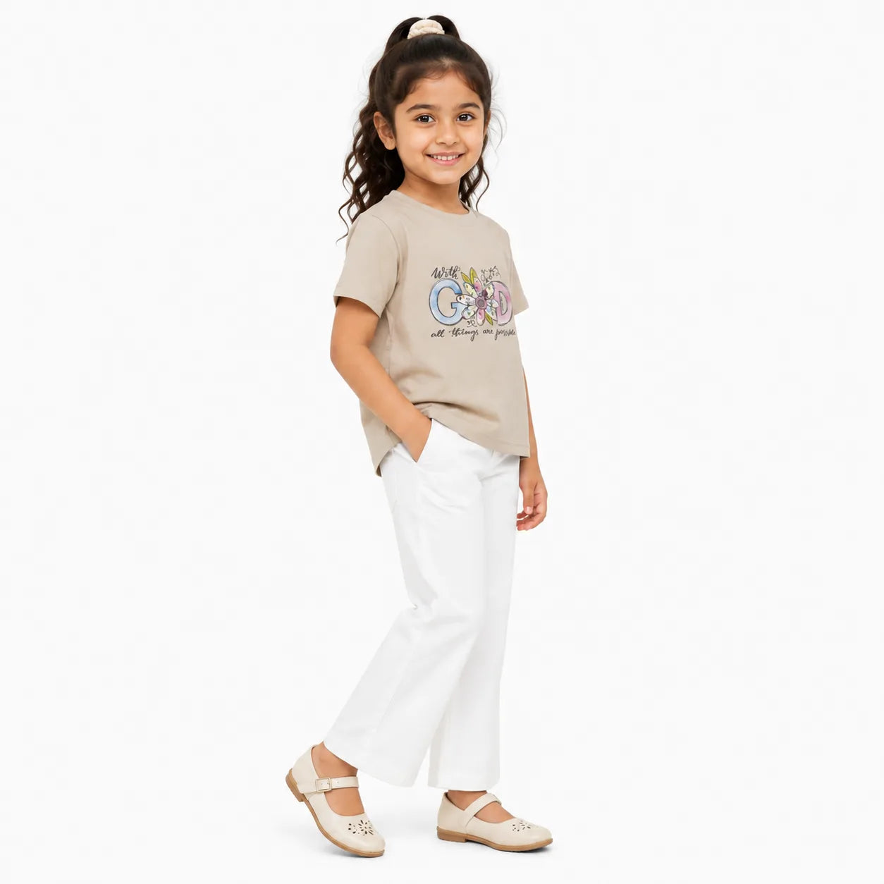 A young girl modeling a beige graphic t-shirt, white wide-leg pants, and beige Mary Jane shoes against a plain white background.